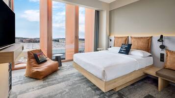 Ein Hotelzimmer mit einem großen Bett, einem Schreibtisch, einem Sessel und Blick auf die Stadt.