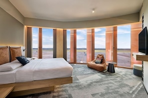 Una habitación de hotel moderna con una cama grande, un sillón de peluche y un televisor.