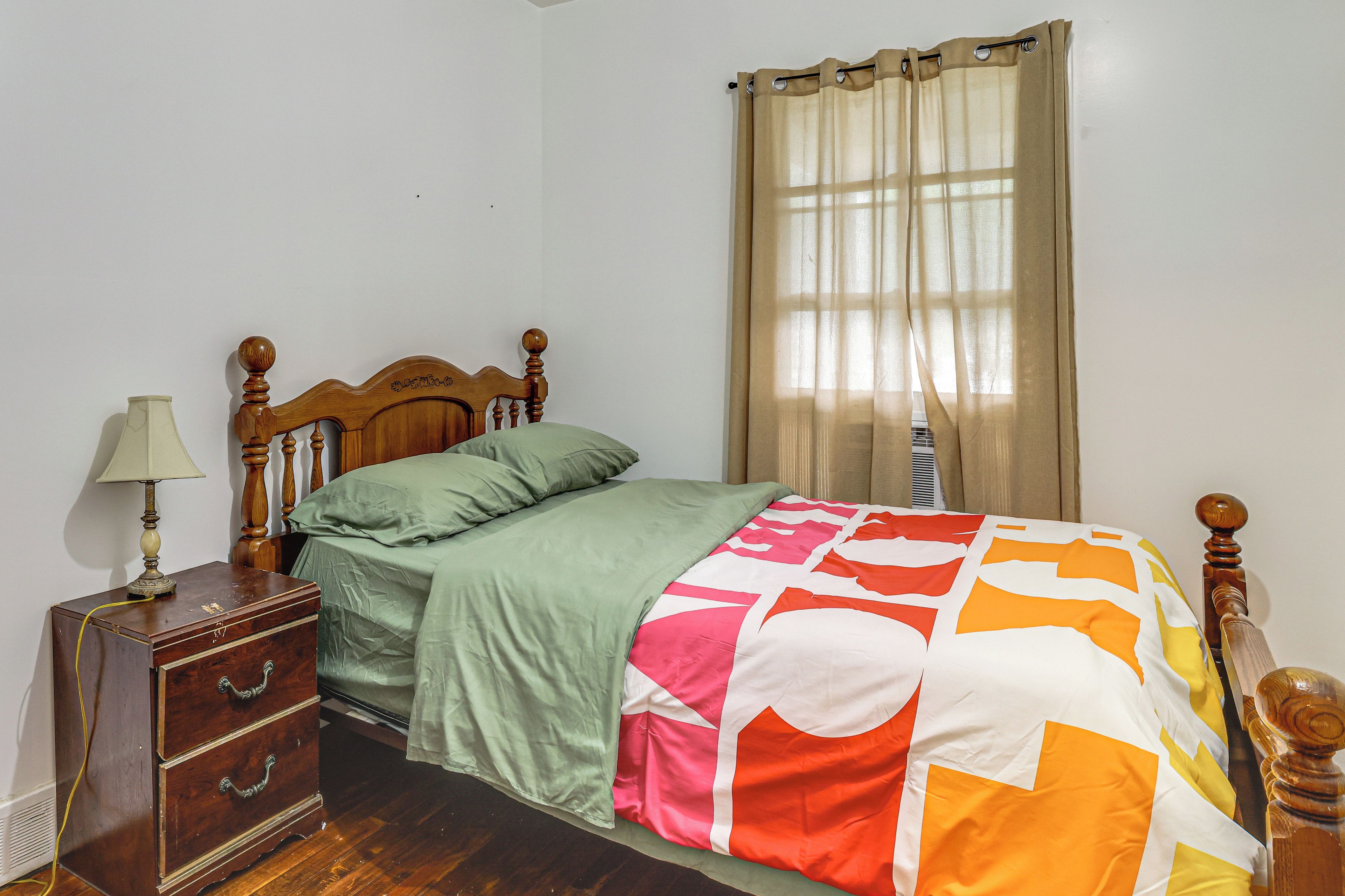 Une chambre à coucher avec un lit en bois, une table de chevet, une lampe, une fenêtre avec des rideaux et un radiateur.