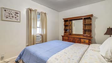 A bedroom with a bed, a dresser, a mirror, a window with curtains, and a wall-mounted air conditioning unit.