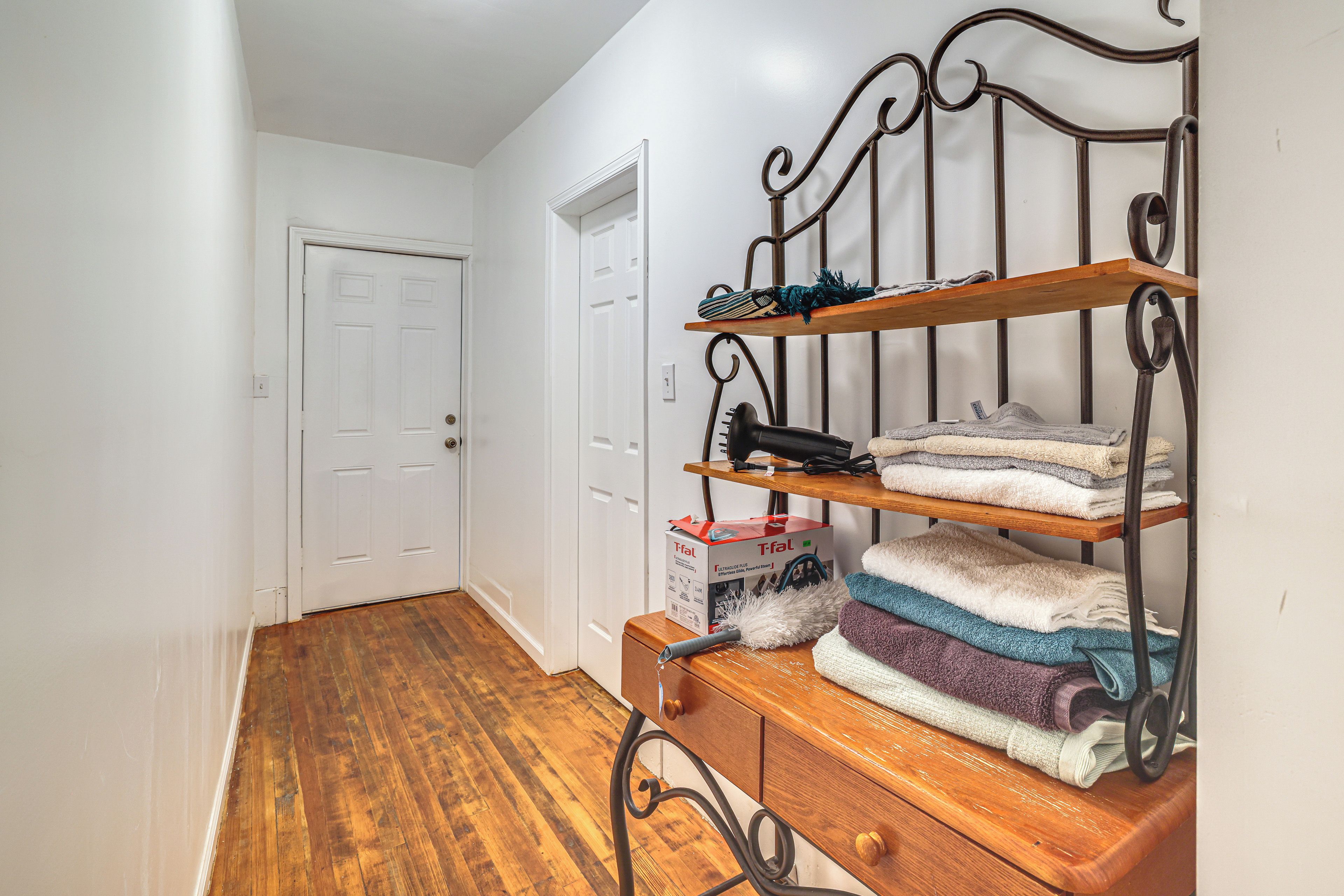 A hallway with a wooden bench, a metal shelf unit with folded towels, and a white door.