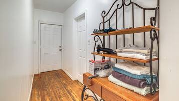 A hallway with a wooden bench, a metal shelf unit with folded towels, and a white door.