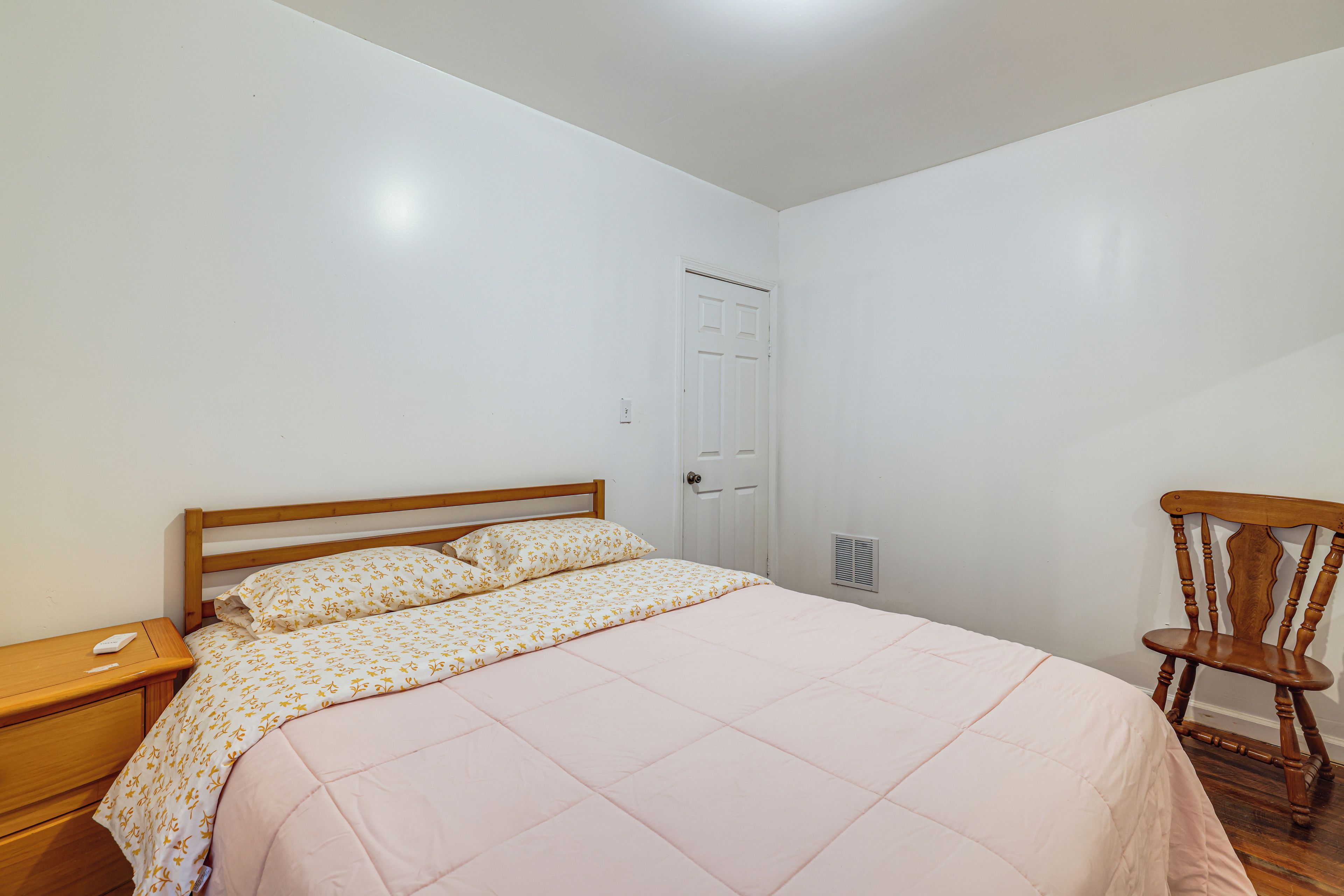 A bedroom with a bed, a wooden nightstand, a chair, and a door.