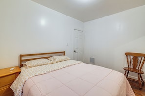 A bedroom with a bed, a wooden nightstand, a chair, and a door. - Easy Niagara Falls Access! Apt w/ Full Kitchen (Niagara Falls)