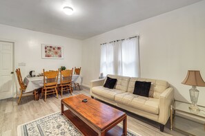 Una sala de estar con sofá, mesa de centro y sillas. Hay una mesa de comedor con sillas y un cuadro en la pared.