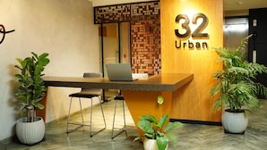 Una recepción con una computadora portátil, dos plantas en macetas y un panel de madera con el número 32 y la palabra 'Urban'.