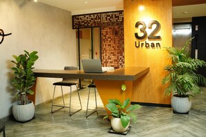 Una recepción con una computadora portátil, dos plantas en macetas y un panel de madera con el número 32 y la palabra 'Urban'.