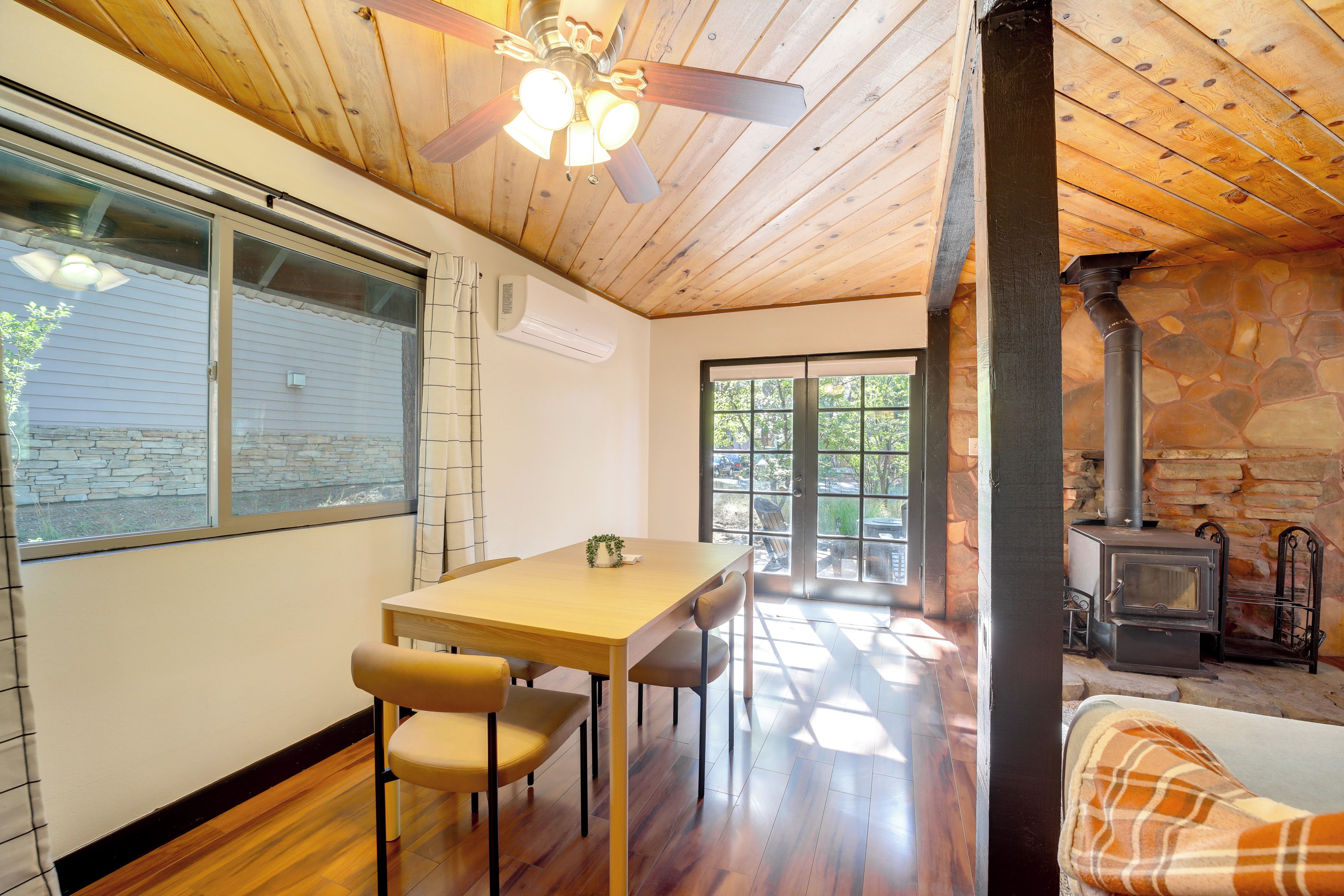 Un interior acogedor con techo de madera, una zona de comedor con mesa y sillas, una chimenea de piedra y vistas a través de un ventanal.
