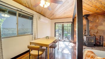Un interior acogedor con techo de madera, una zona de comedor con mesa y sillas, una chimenea de piedra y vistas a través de un ventanal.