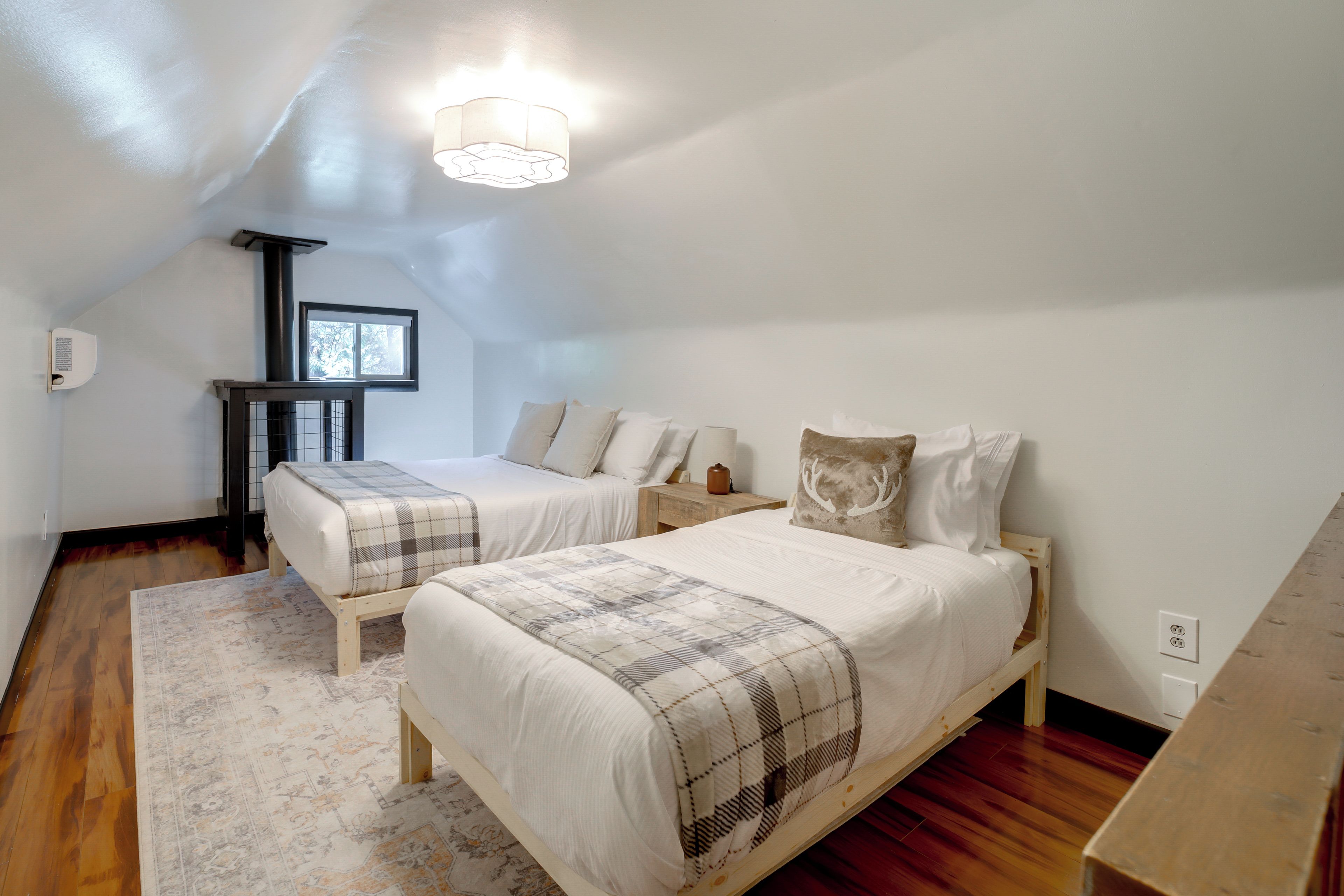 A bedroom with two beds, a window, a radiator, and a wooden floor.