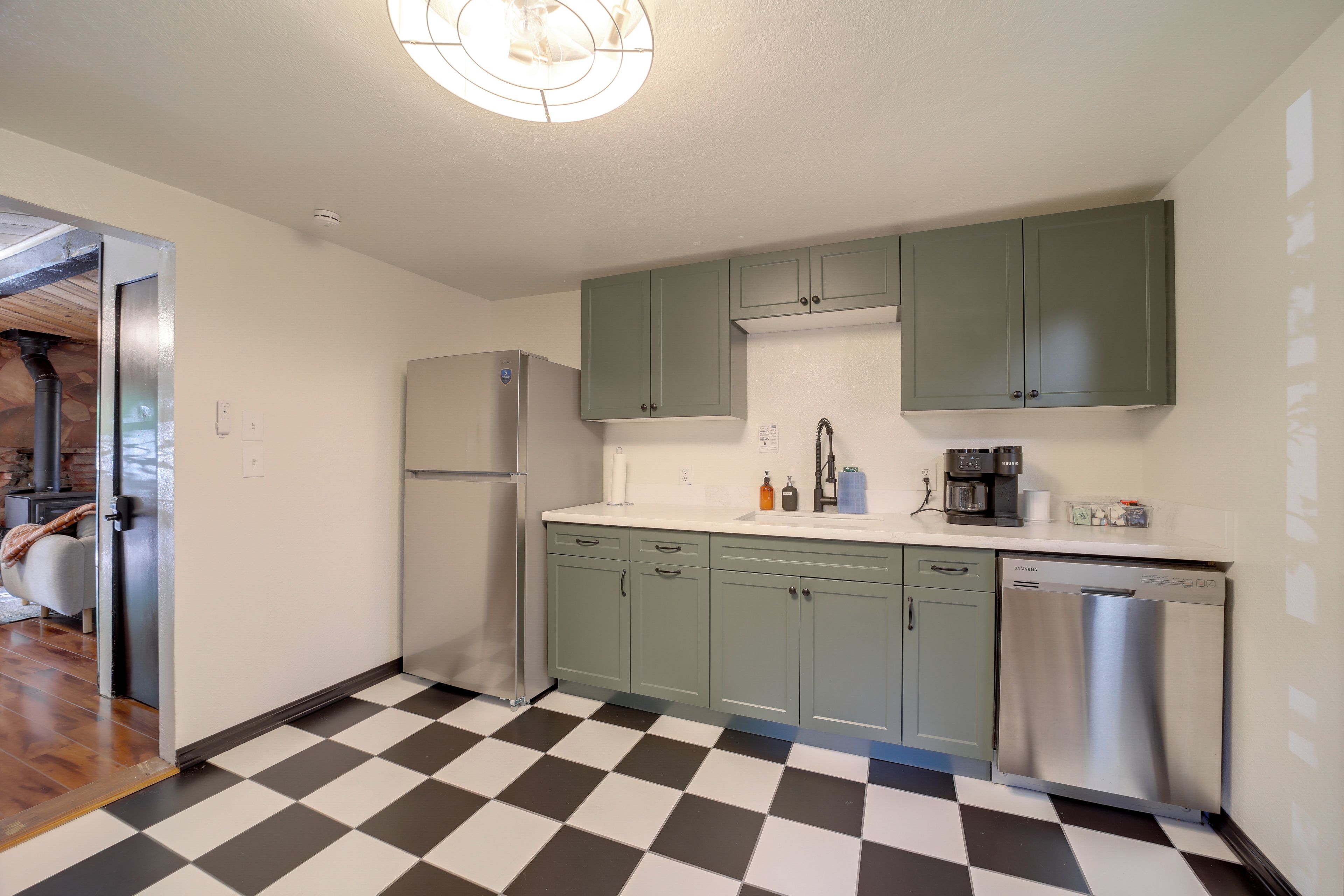 A kitchen with a checkered floor, a refrigerator, a dishwasher, and green cabinets.