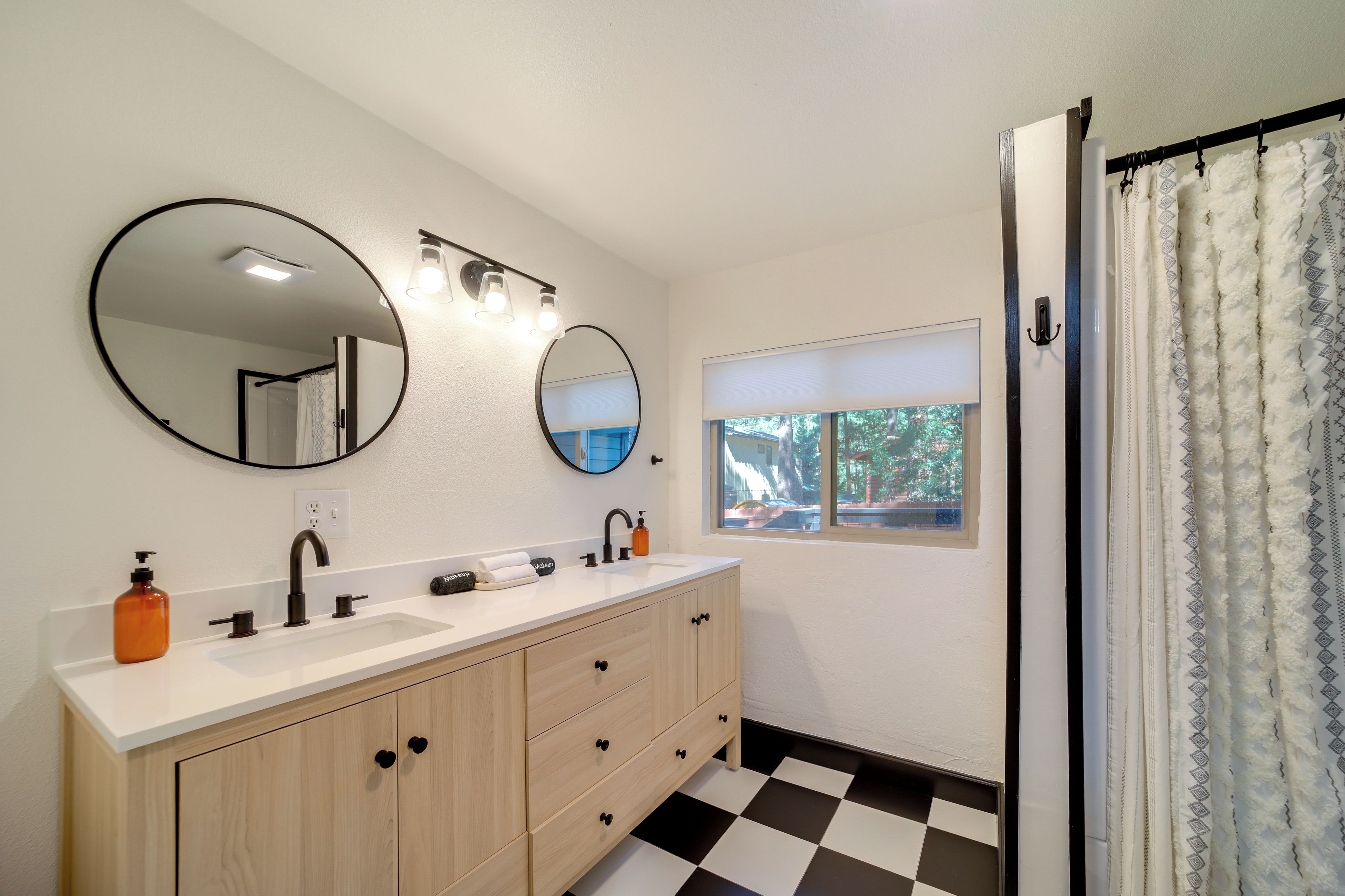 A bathroom with a double sink vanity, two mirrors, a window, and a shower curtain.