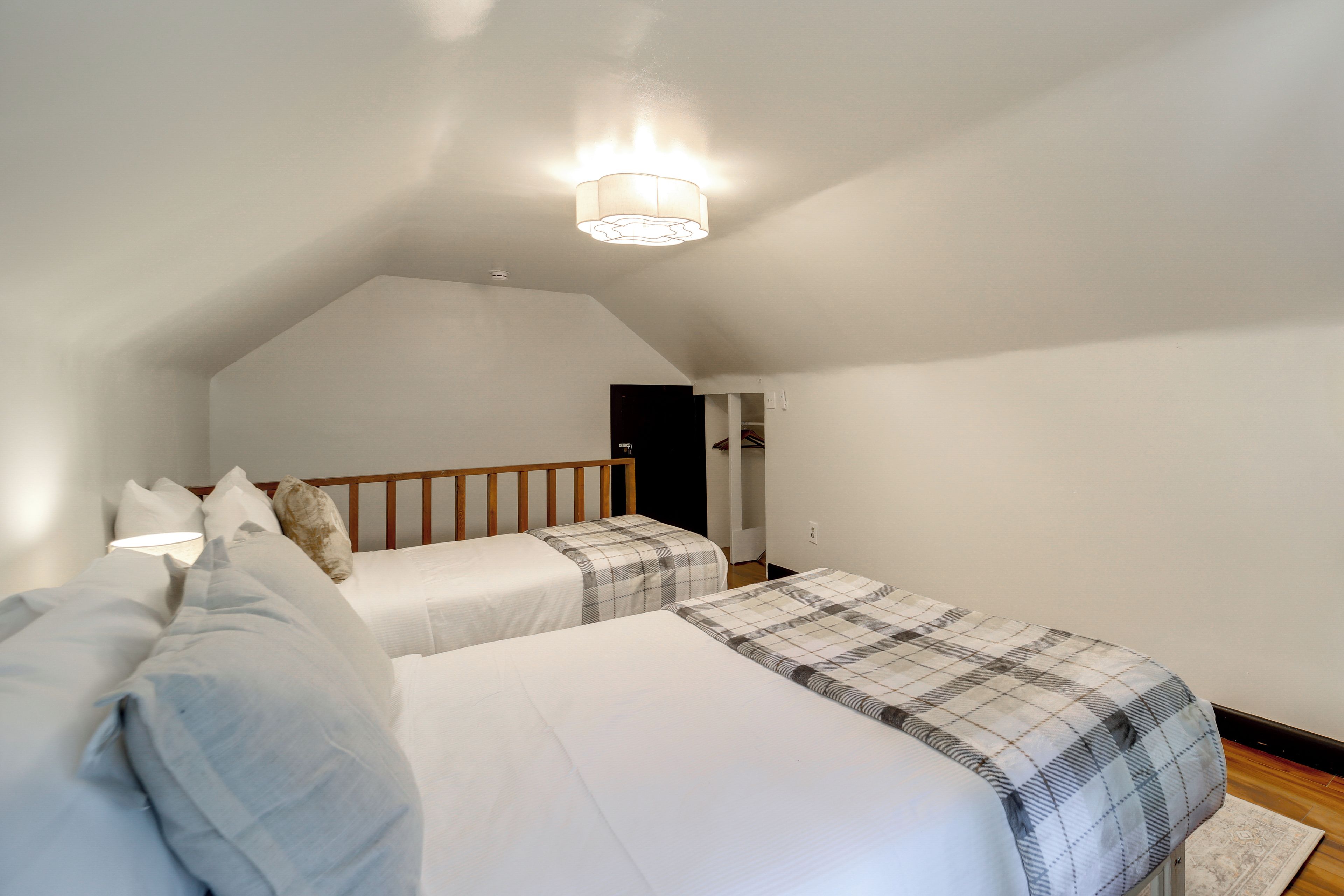 Un dormitorio con dos camas, cabecero de madera, lámpara de techo y una puerta que da a otra habitación.
