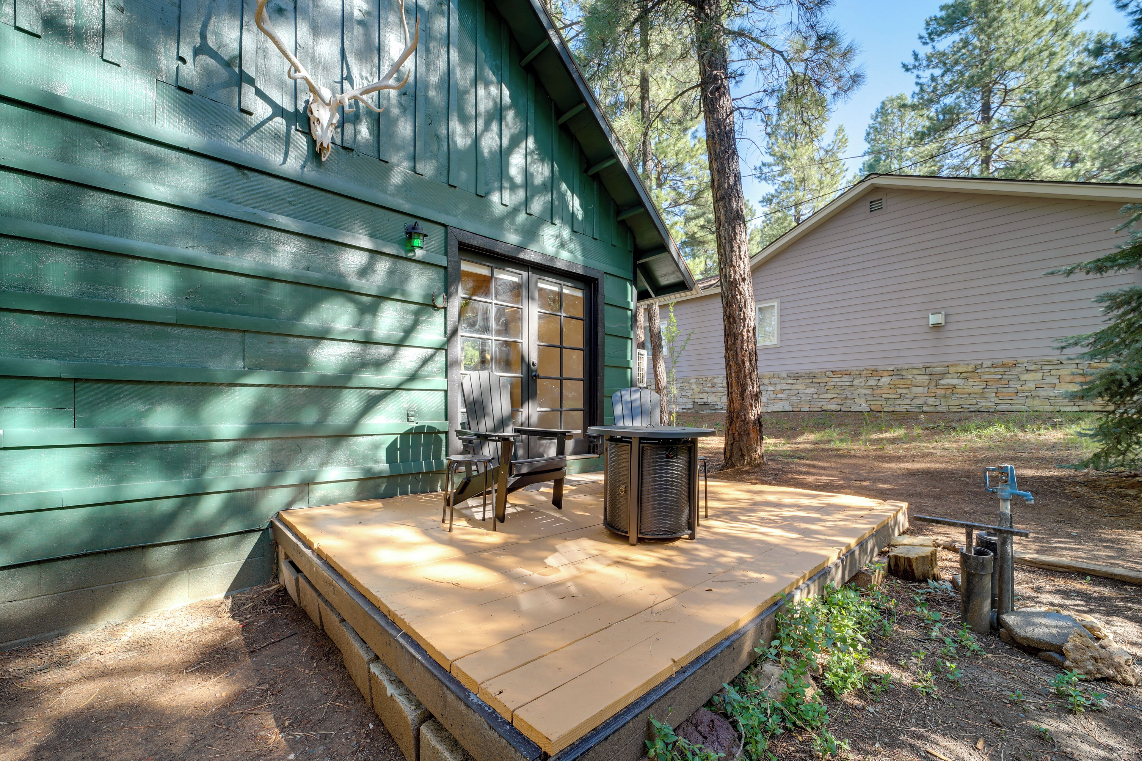 A wooden deck with a table and chairs, a stone wall, and a building with a green facade.