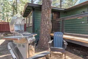 An outdoor grill area with a metal grill, a wooden bench, and a chair. - Hotevilla Hideaway, Cozy Cabin Retreat (Flagstaff)