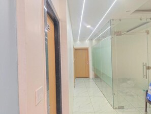 A hallway with a door, a glass partition, and a tiled floor. - Hotel Bhagya (Bhopal)