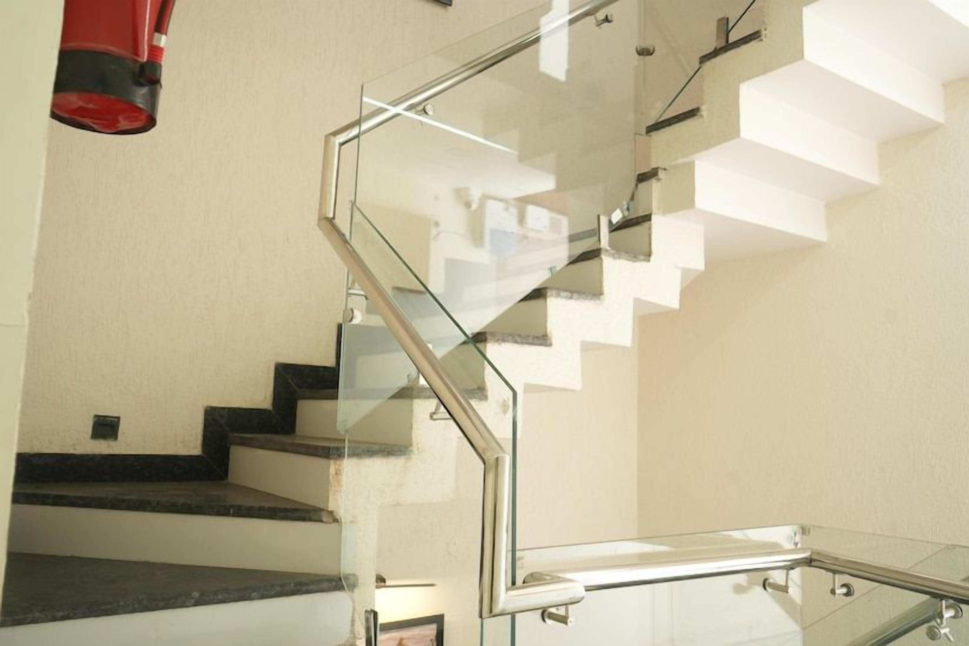 Uma escadaria moderna com guarda-corpos de vidro e um objeto vermelho pendurado no teto.