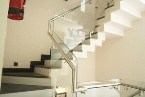 Una escalera moderna con barandas de vidrio y un objeto rojo colgando del techo.