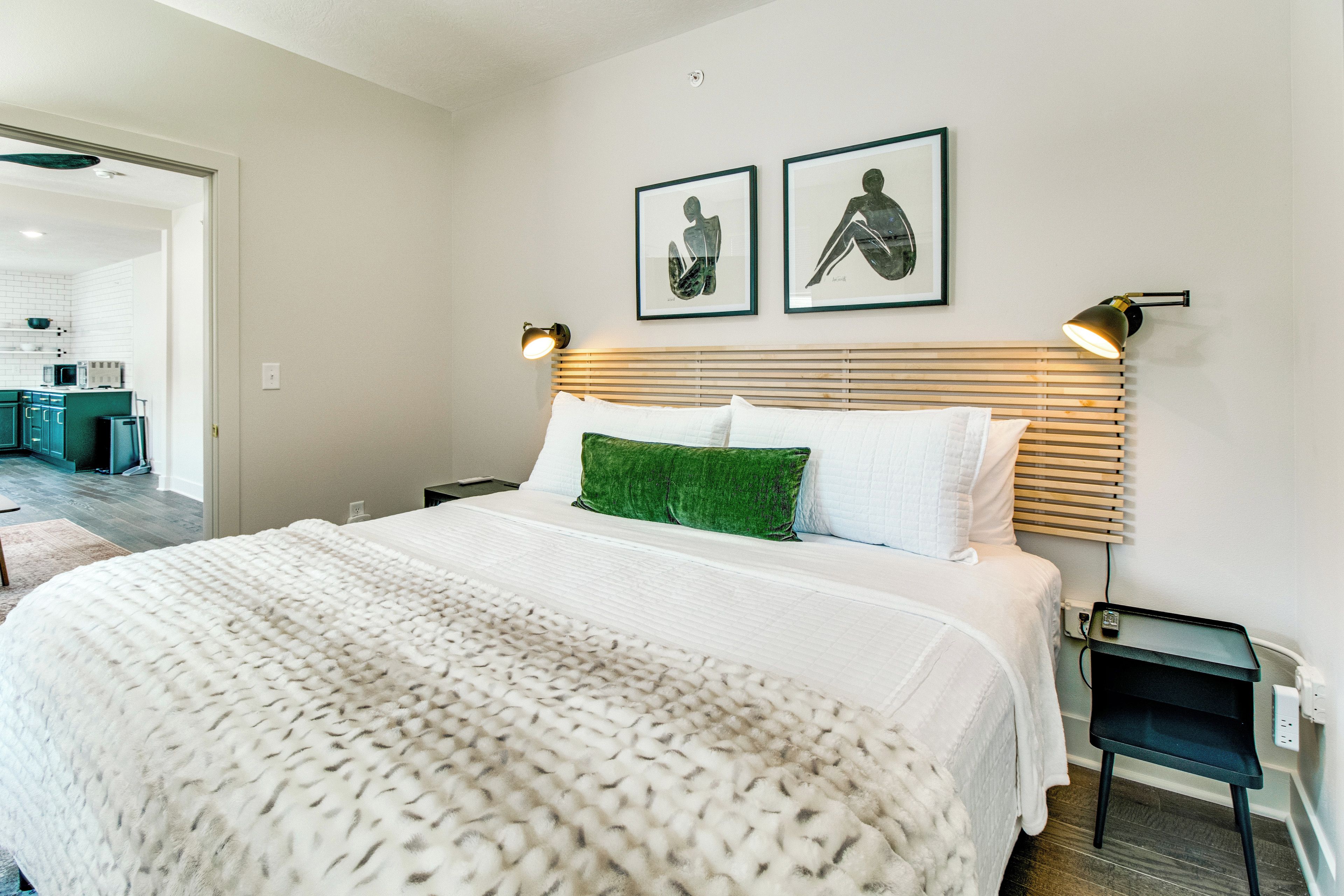 A hotel room with a large bed, a green throw pillow, and two framed artworks on the wall.