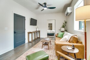 A modern living room with a sofa, a coffee table, a small table with a lamp, a ceiling fan, and a TV mounted on the wall.