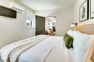 A bedroom with a bed, a bedside table, a lamp, and a door leading to a bathroom.