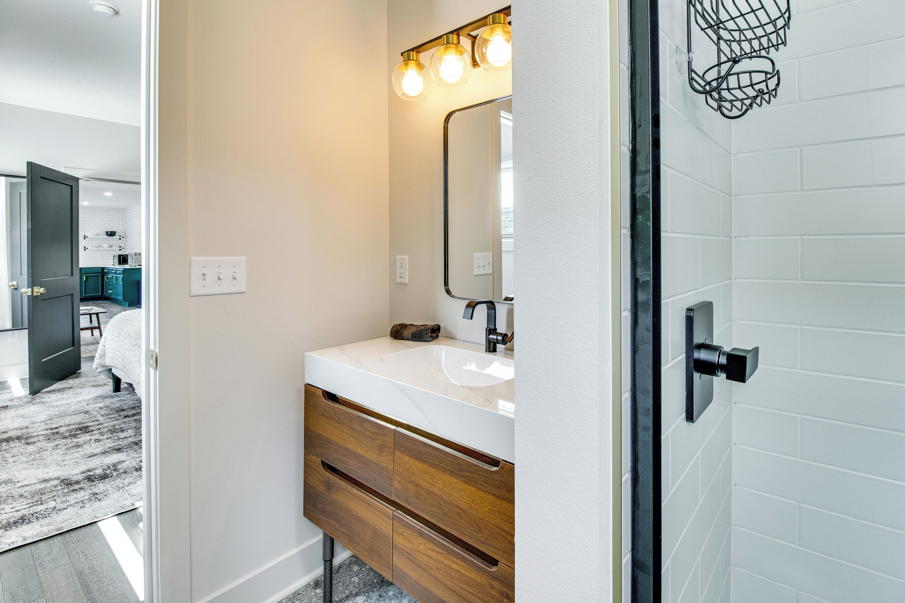A modern bathroom with a white sink, wooden vanity, and a mirror with three lights.