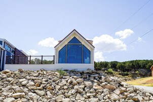 Un edificio moderno con una llamativa fachada de vidrio azul, ubicado en una colina rocosa bajo un cielo despejado.