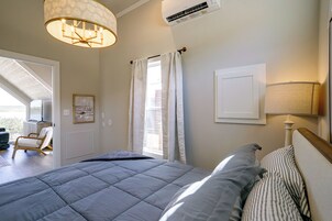 Un dormitorio con una cama grande, una lámpara en el techo, una ventana con cortinas, un aire acondicionado instalado en la pared y un cuadro enmarcado.