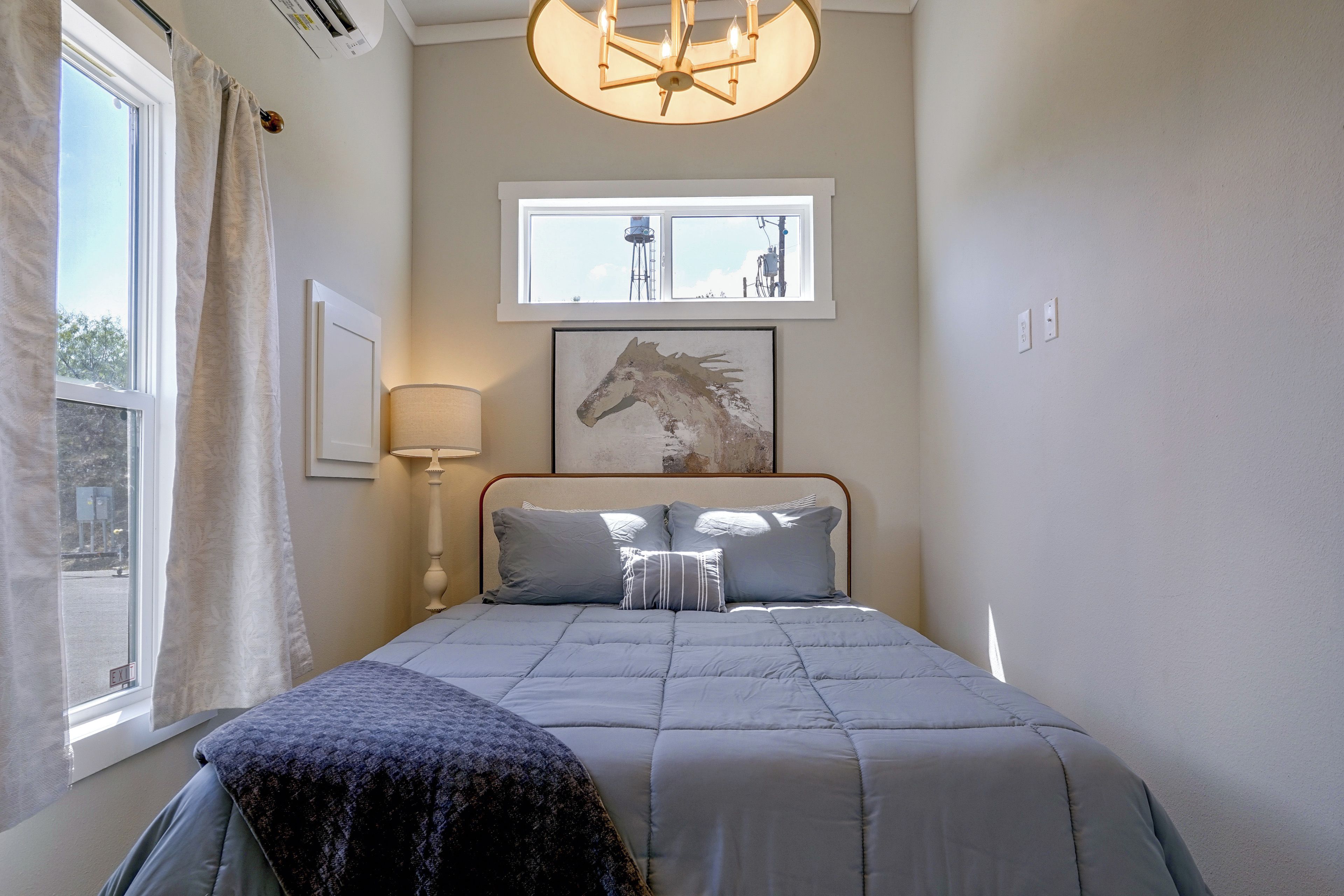 Un dormitorio con cama, ventana, lámpara y un cuadro colgado en la pared.