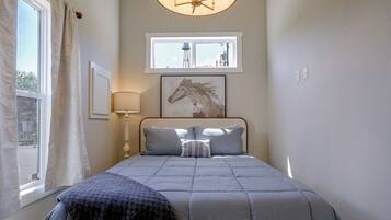 Un dormitorio con cama, ventana, lámpara y un cuadro colgado en la pared.