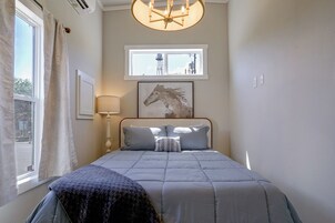 Un dormitorio con cama, ventana, lámpara y un cuadro colgado en la pared.