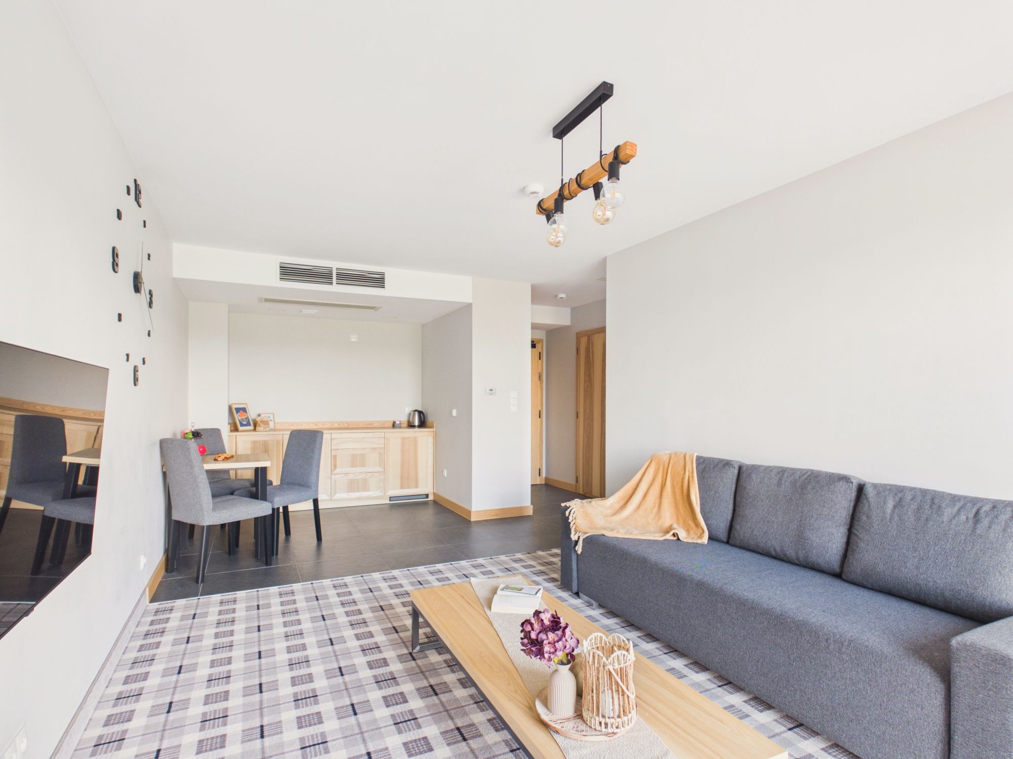 Una sala moderna con un sofá gris, una mesa de centro de madera y una alfombra estampada.