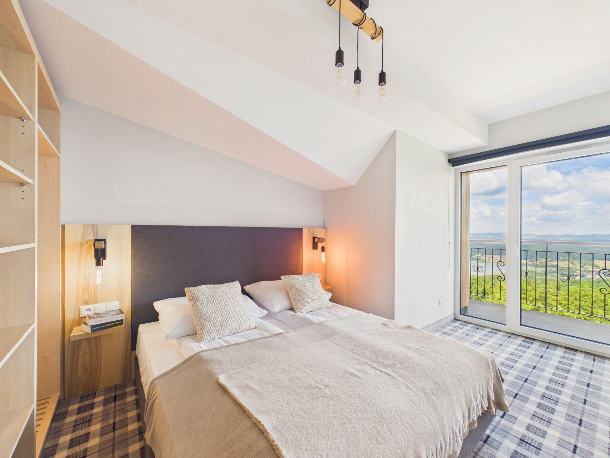 A bedroom with a bed, bedside tables, a nightstand, a window with a view, and a ceiling light fixture.