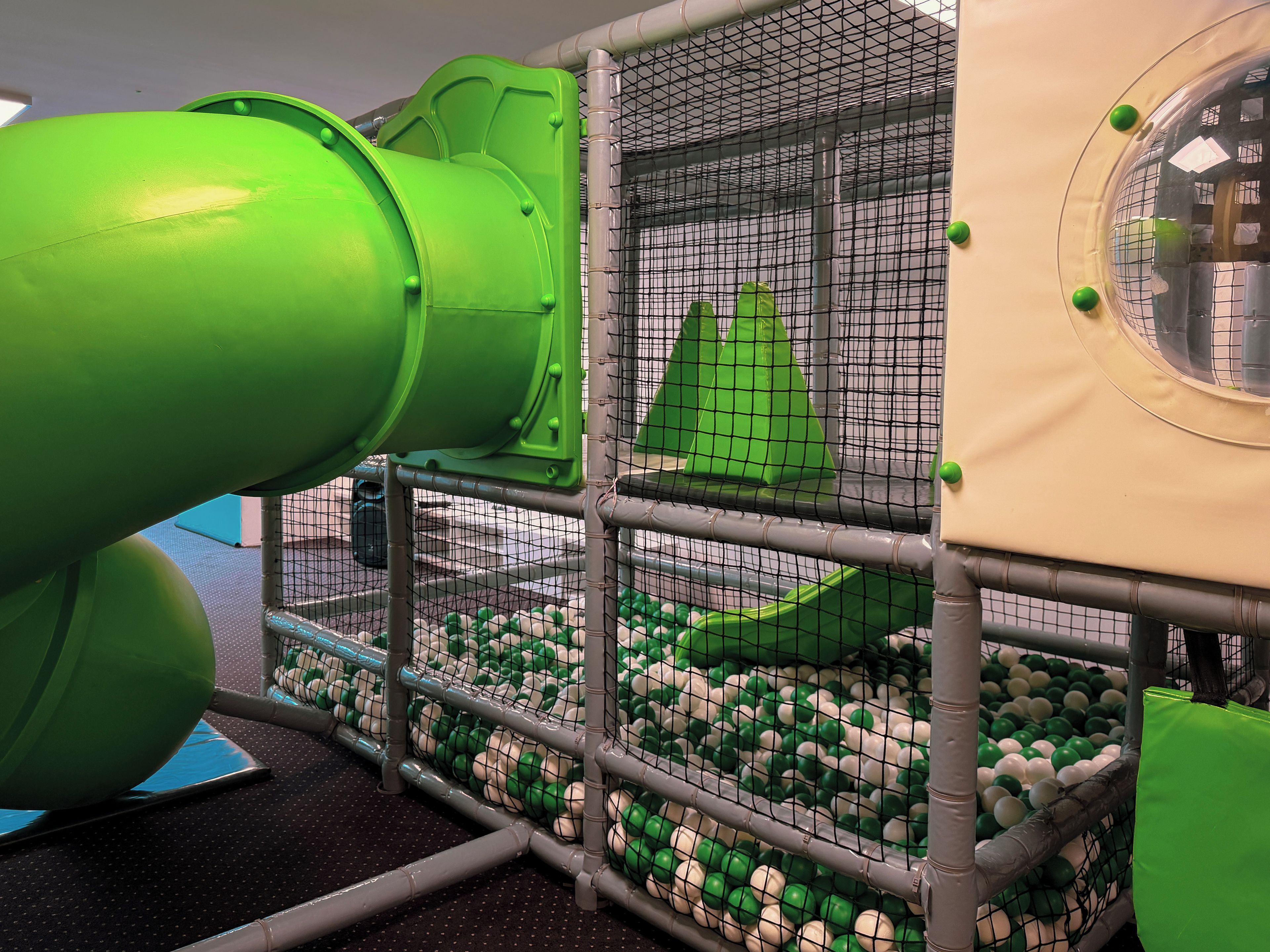 Un área de juegos con un tobogán, paredes de malla y una piscina de pelotas.