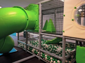 A play area with a slide, netted walls, and a ball pit. - Kazalnica Family & Conference Resort with Pool & Restaurant by Solarento (SosnĂłwka)