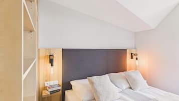 Un dormitorio con cama, almohadas, una mesita de noche, un libro e iluminación en la pared.