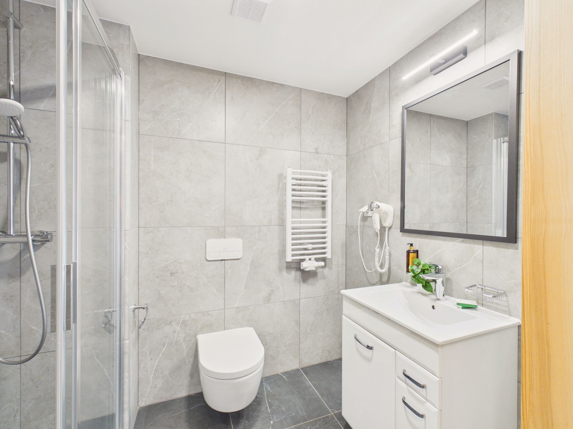 Un baño moderno con cabina de ducha de vidrio, inodoro blanco, tocador con espejo y barra para toallas.