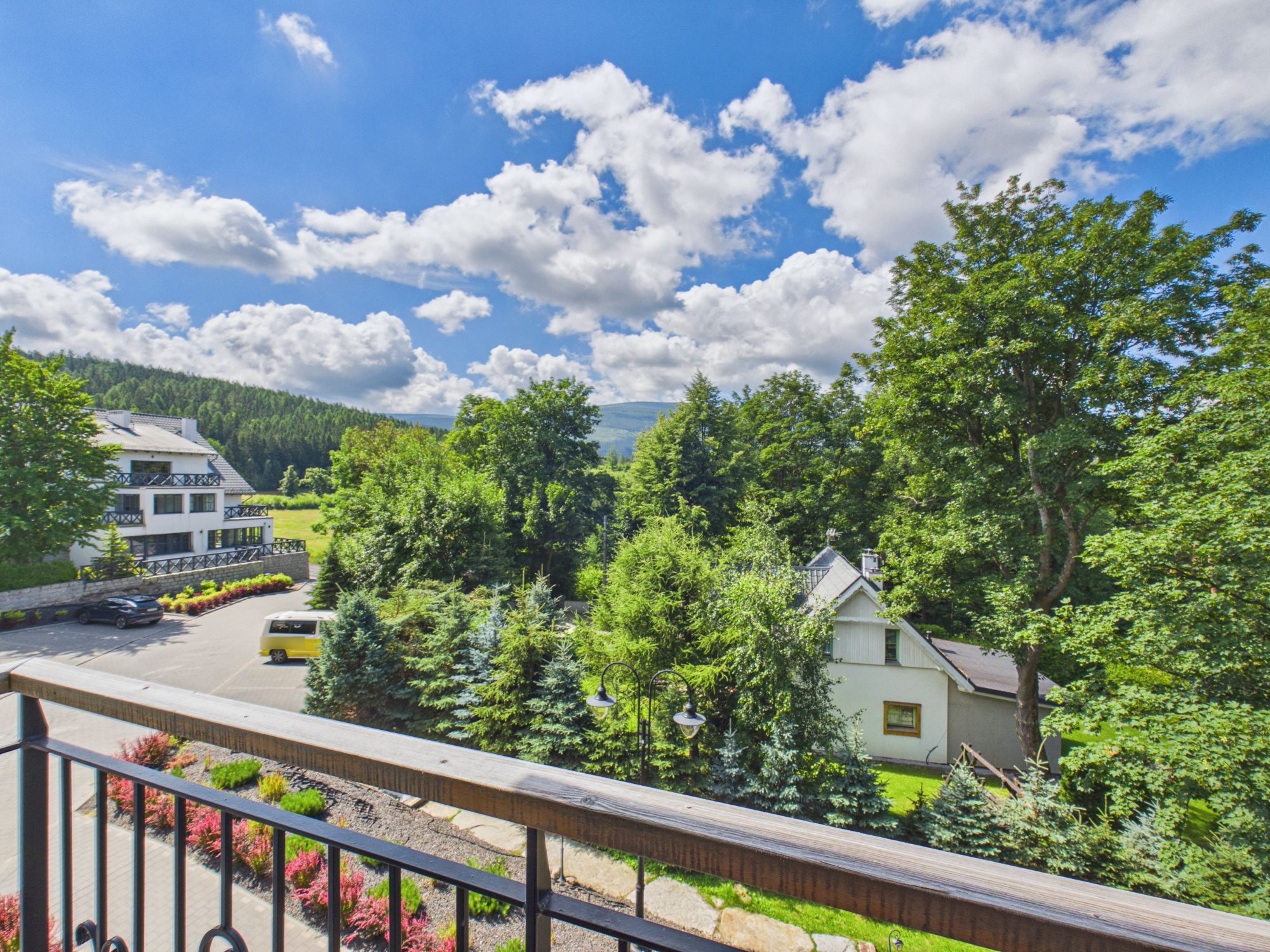 A residential area with a white house, a parking lot, and a view of a forested mountain range.