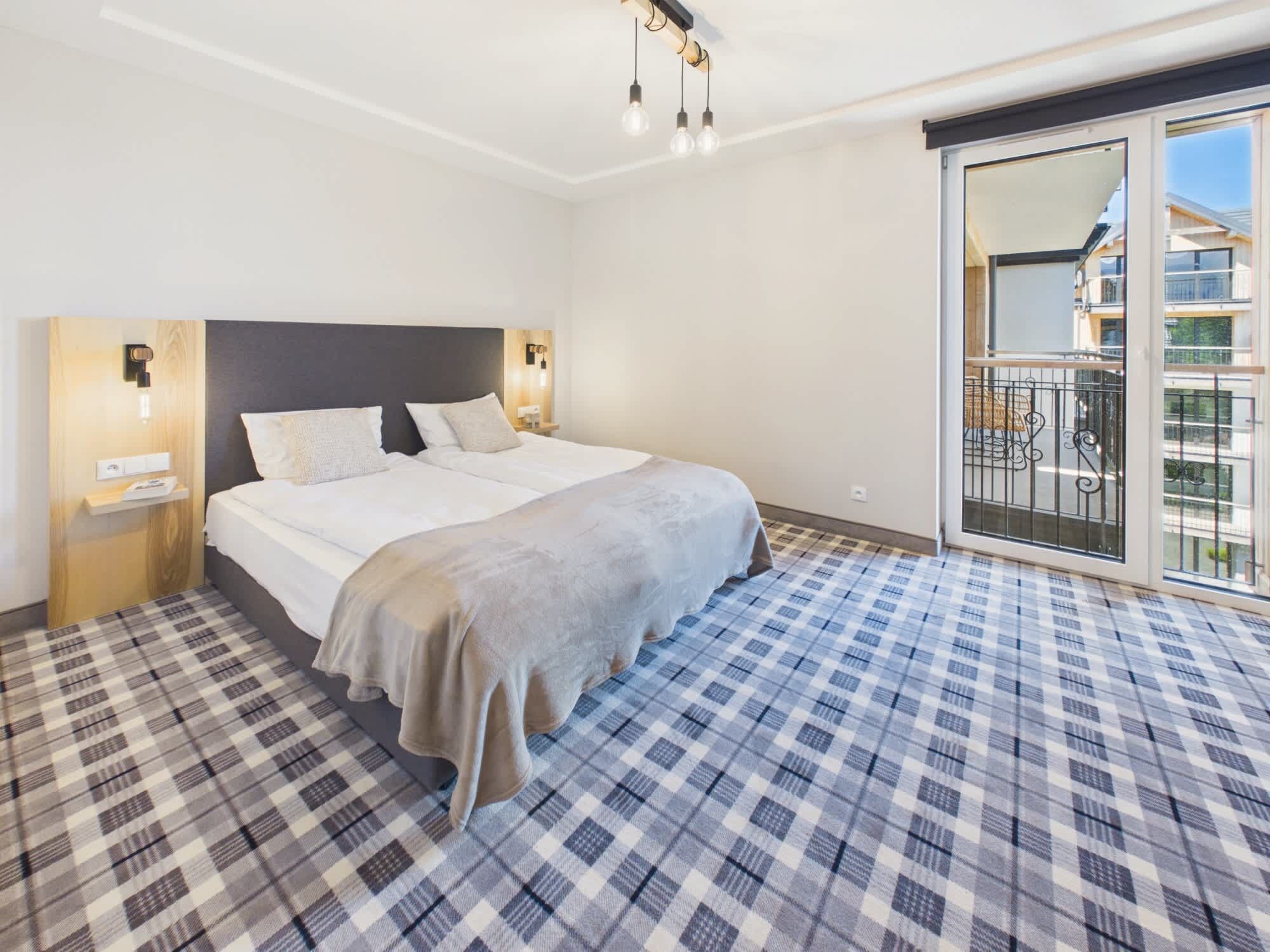 Habitación de hotel con una cama grande, piso a cuadros, balcón con vistas y una lámpara moderna.