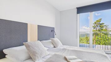 Un dormitorio moderno con una cama grande, vistas a la vegetación por la ventana y un balcón con barandilla.