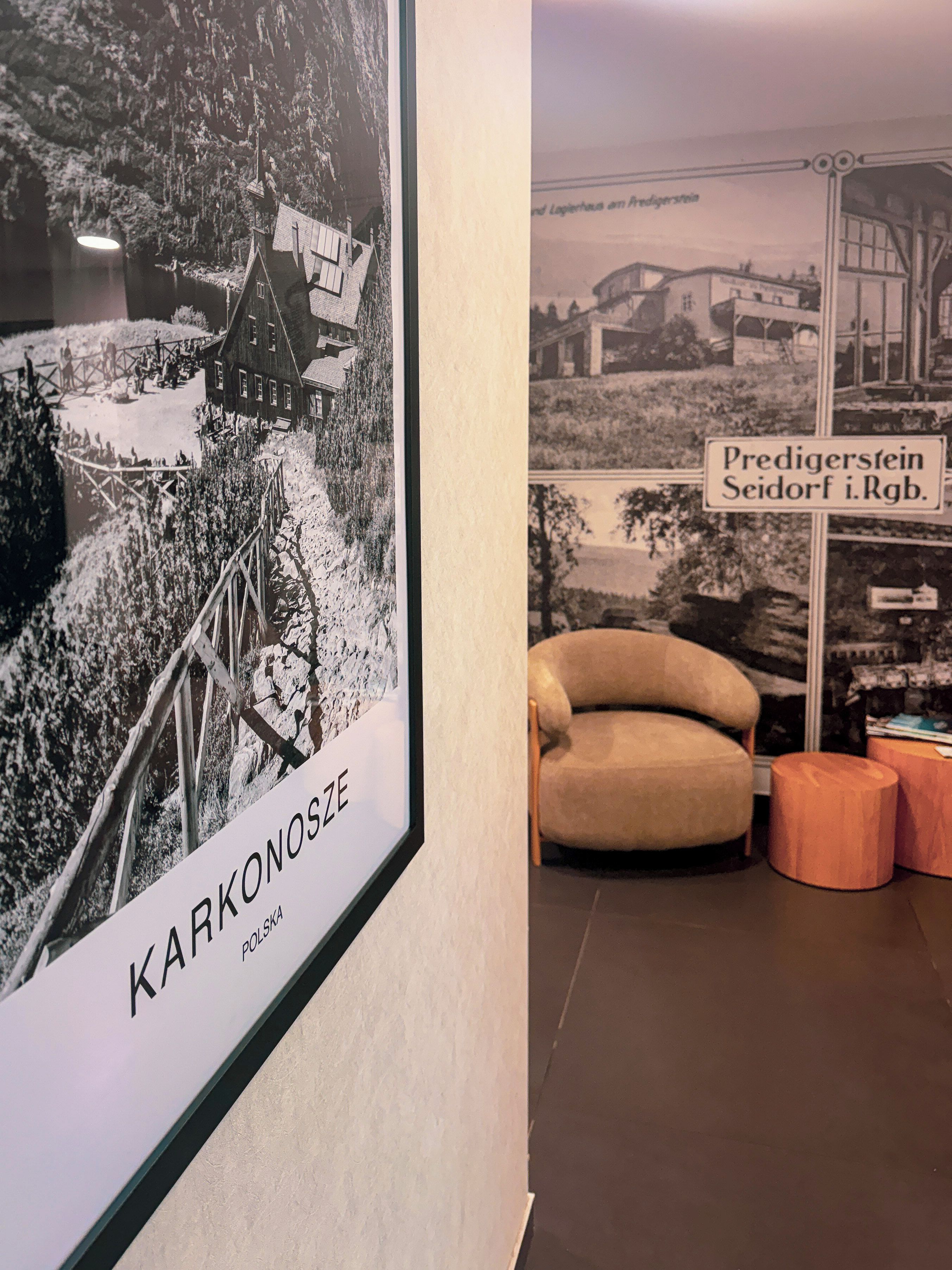 Fotografía antigua enmarco de una escena de pueblo con un cartel que dice 'KARKONOSZE POLSKA' y una silla en primer plano.