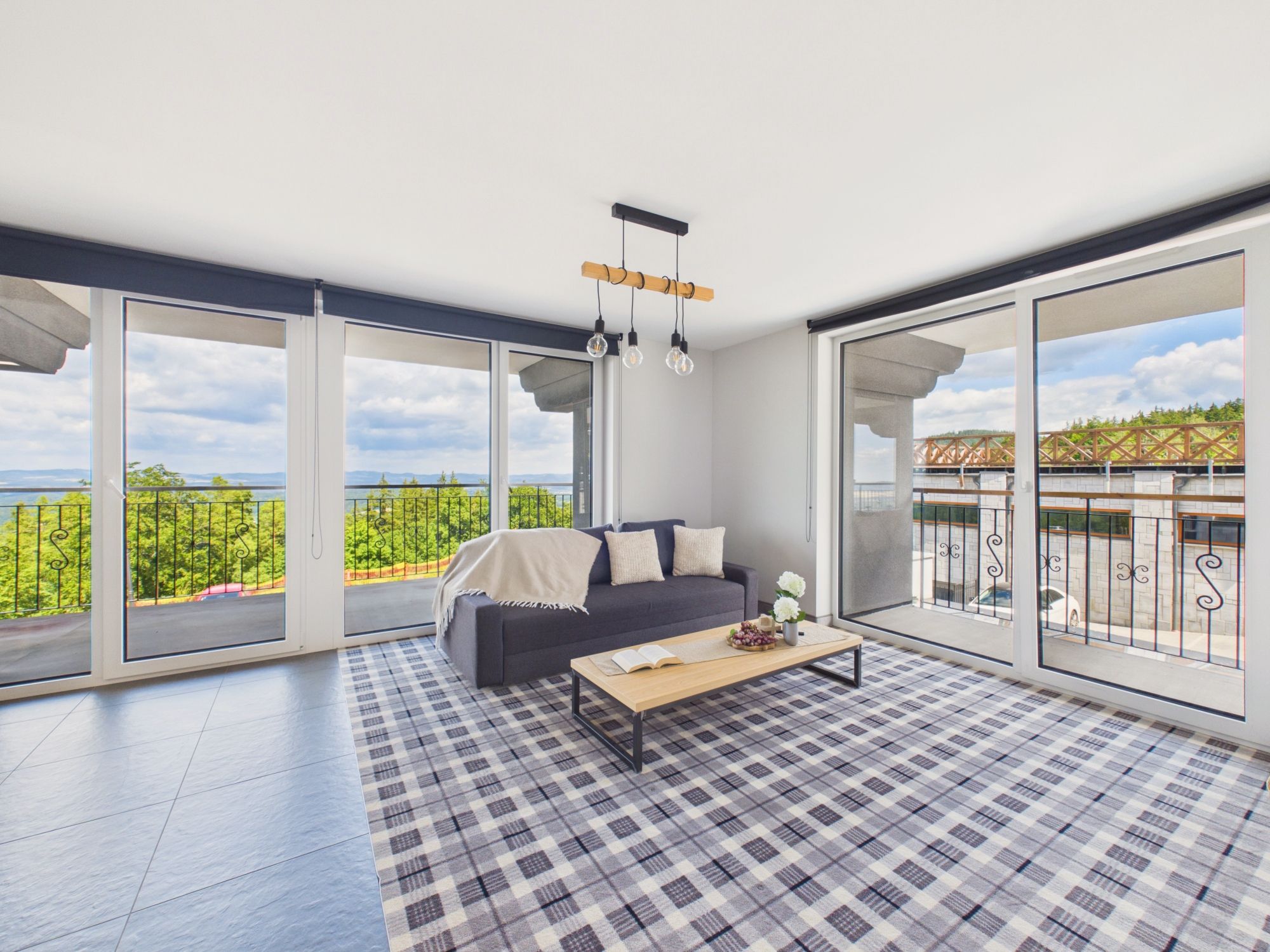 A spacious balcony with a sofa and coffee table, large windows offering a scenic view, and a checkered floor.