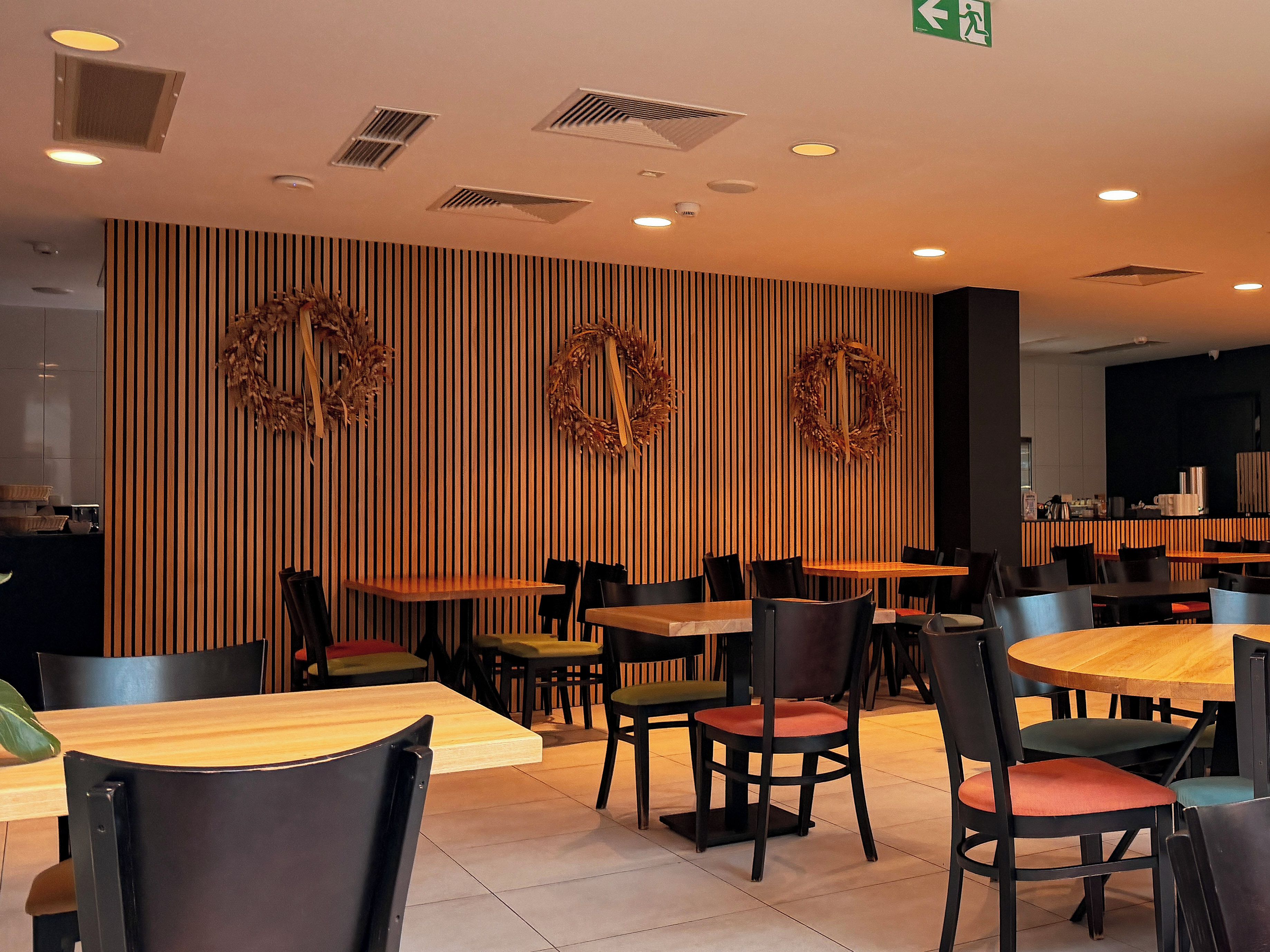 A restaurant interior with wooden panel walls, multiple tables and chairs, and decorative wreaths.
