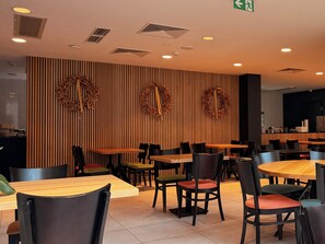 A restaurant interior with wooden panel walls, multiple tables and chairs, and decorative wreaths.