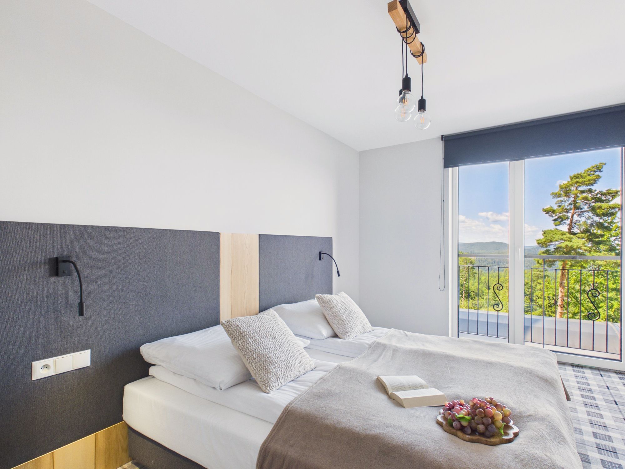 Une chambre moderne avec un grand lit, une vue sur la verdure par la fenêtre et un balcon.