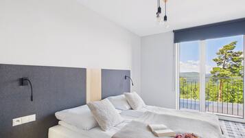 Ein modernes Schlafzimmer mit einem großen Bett, Blick ins Grüne durch das Fenster und einem Balkon.