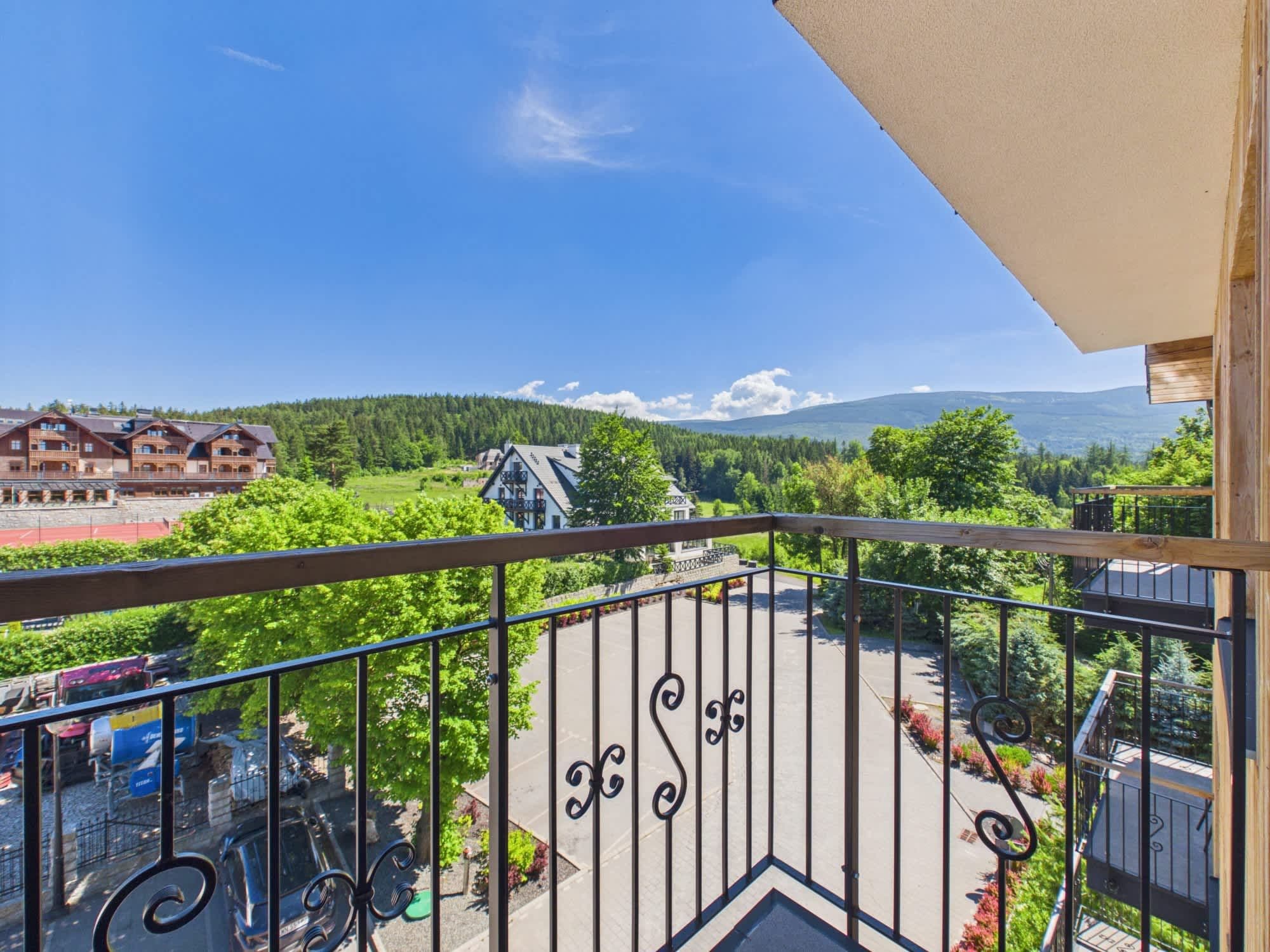 A balcony with a view of a mountainous landscape, a parking area, and a building with a sloped roof.