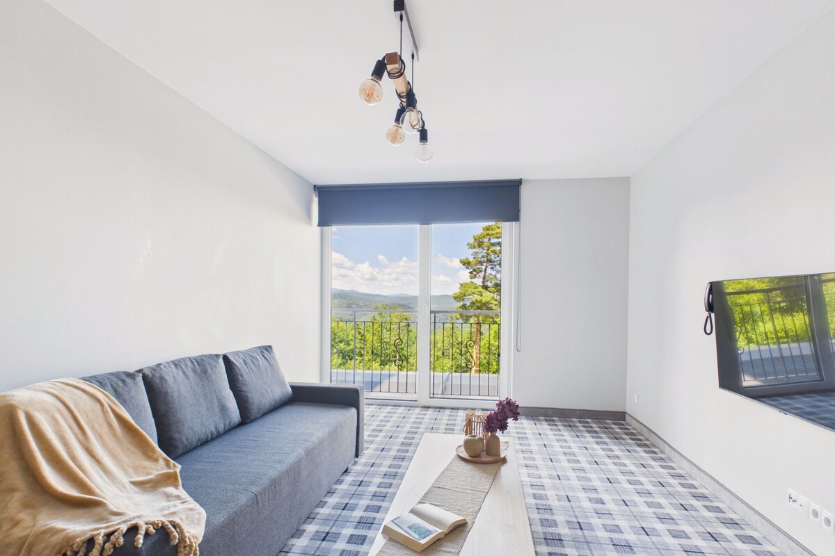 Een moderne woonkamer met een bank, een bijzettafeltje en uitzicht op een balkon met een hekwerk.