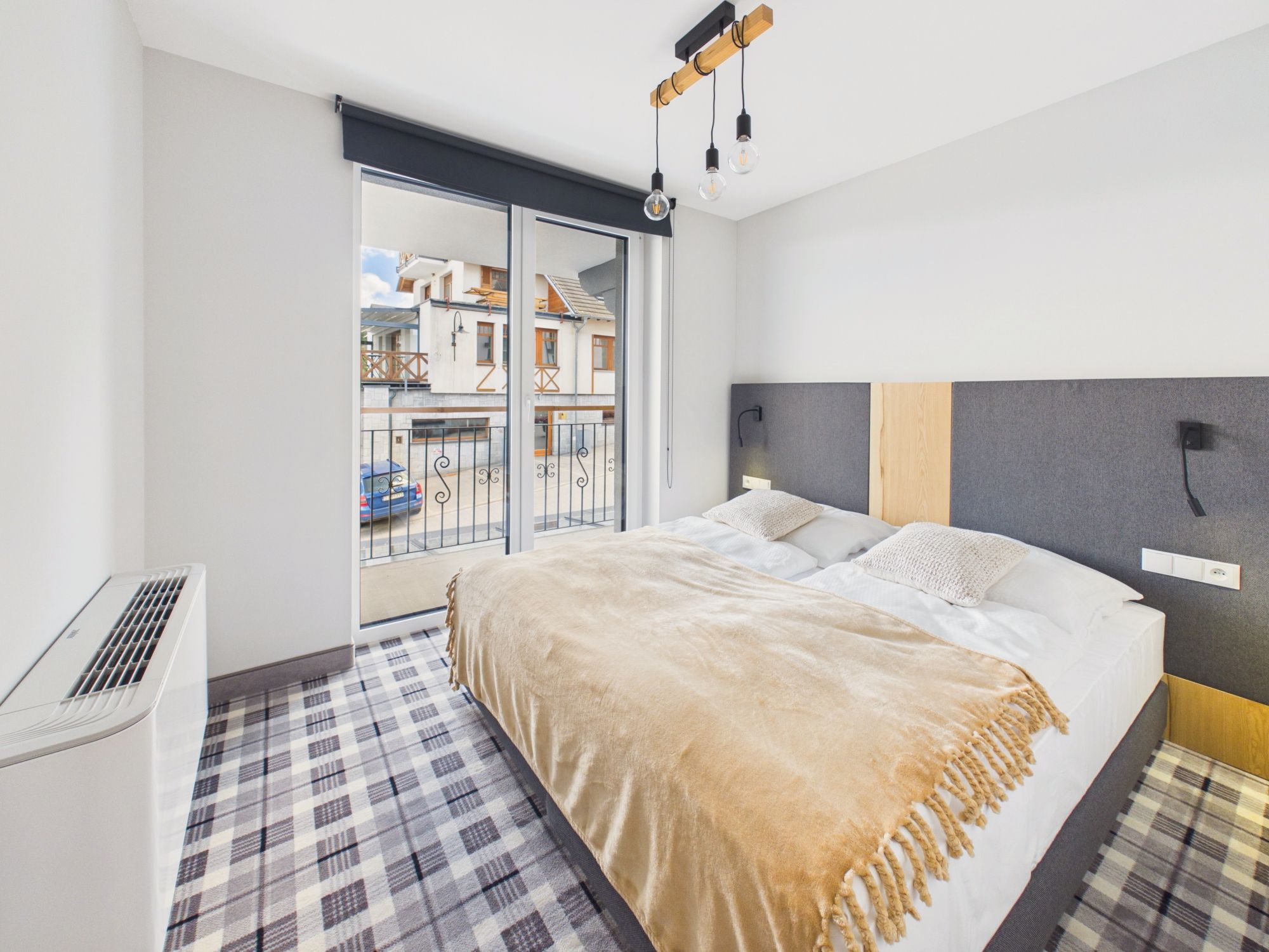 Un dormitorio moderno con una cama grande, una ventana con vistas a edificios y una lámpara en el techo.