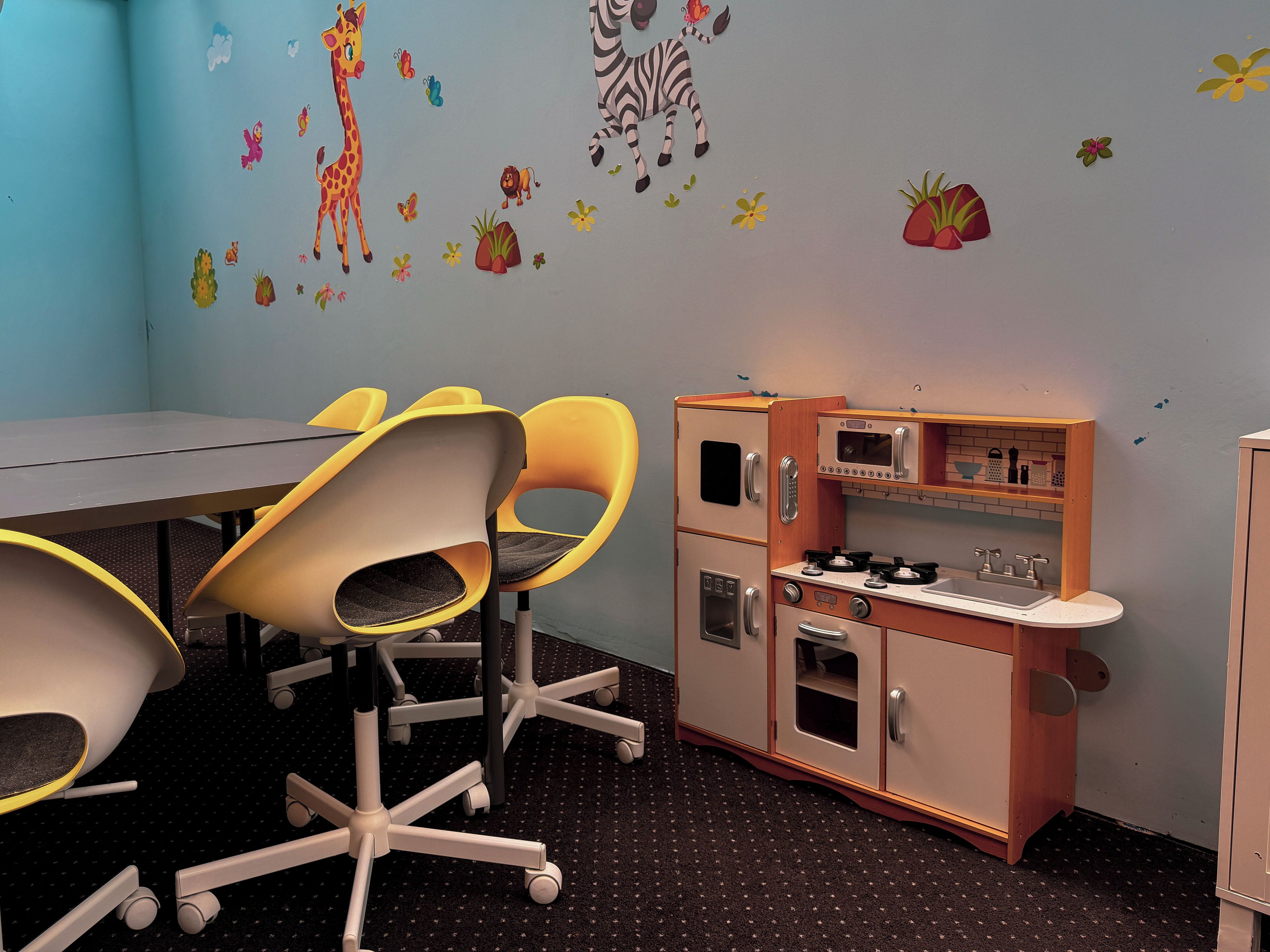 A room with a table, chairs, a kitchenette, and wall decorations.
